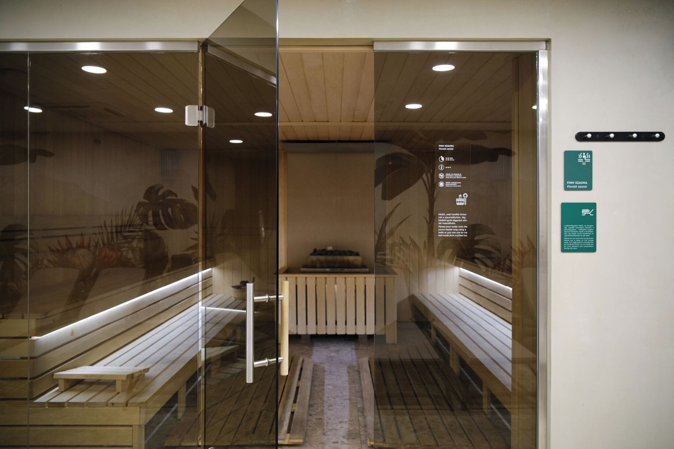 Un cuarto de sauna con bancos, puerta de vidrio, suelo de madera y luces en el techo.