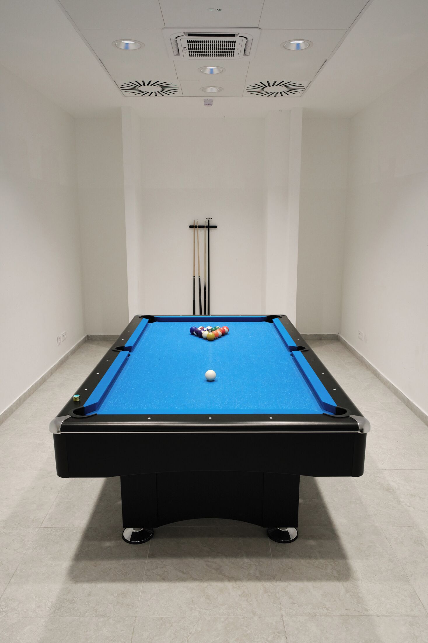 A pool table with balls, a cue stick rack, and a ceiling with ventilation.