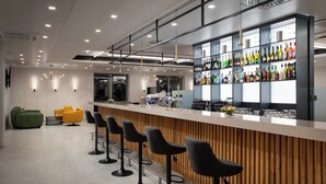 A modern bar with a wooden counter, black bar stools, and a variety of bottles and glasses on shelves. - Hunguest Hotel Flora (Eger)