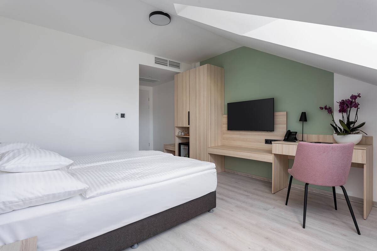 Habitación de hotel moderna con cama, escritorio, silla, televisor y planta en maceta.