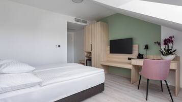 A modern hotel room with a bed, desk, chair, TV, and a potted plant.