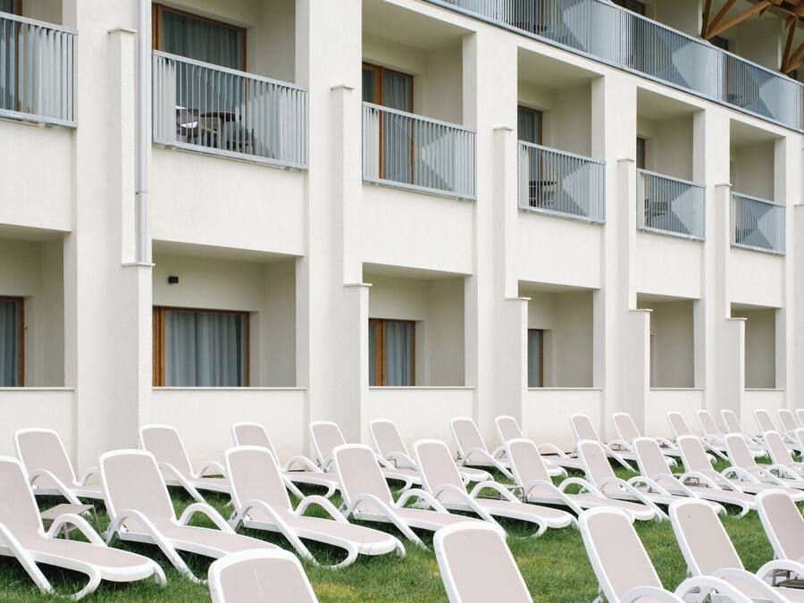 Un hotel con varios balcones, sillones blancos para lounge y un estilo arquitectónico moderno.