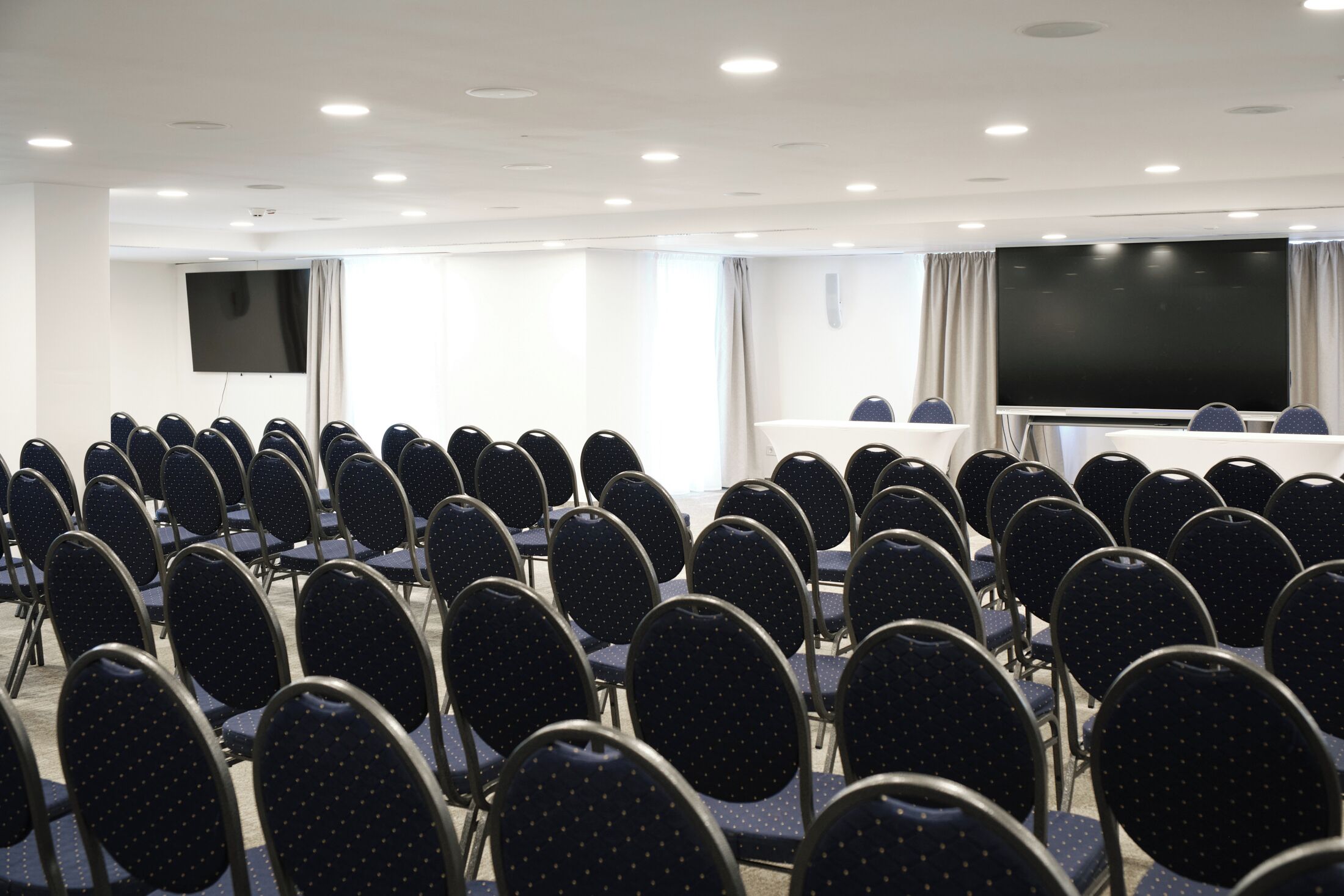 Ein Konferenzraum mit Stuhlreihen, einer großen Leinwand und einem Tisch.