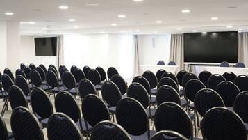 Ein Konferenzraum mit Stuhlreihen, einer großen Leinwand und einem Tisch.