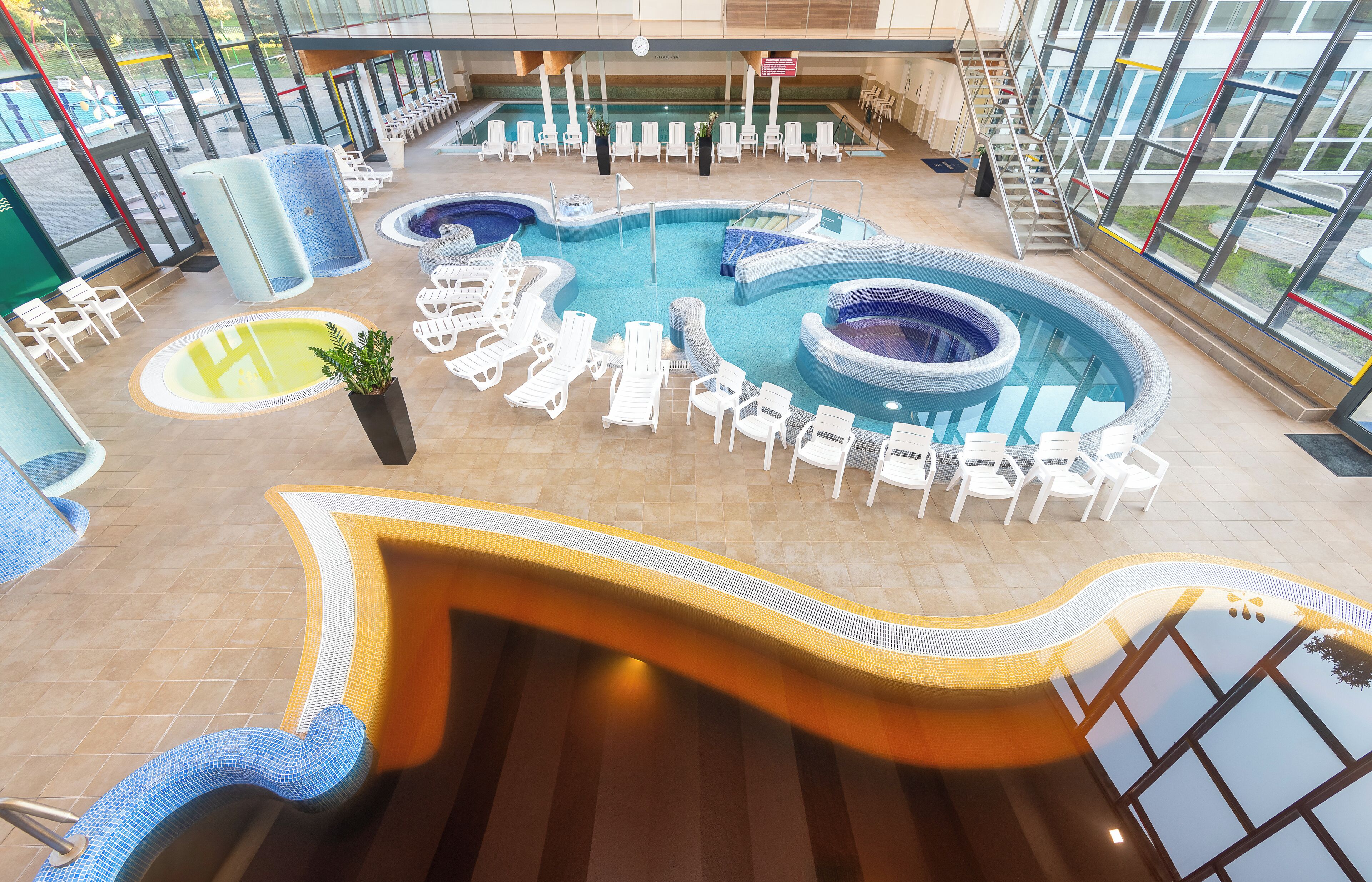 Una amplia piscina cubierta con varias pistas, sillones de descanso y una solárium.