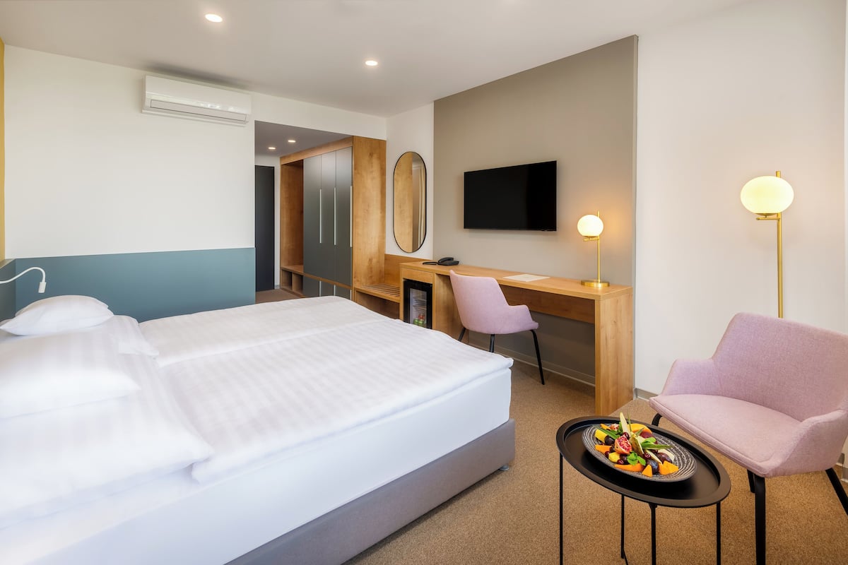 Quarto de hotel com cama, escrivaninha, cadeira, televisão e uma pequena mesa com fruta.