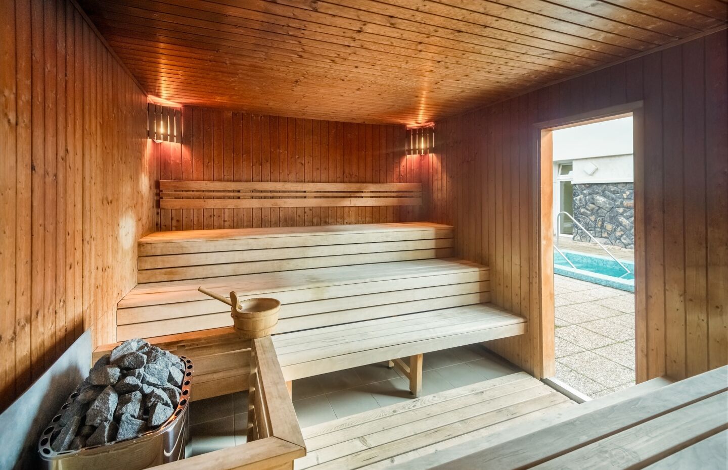 A sauna with wooden benches, a bucket of stones, and a small table with a pot.