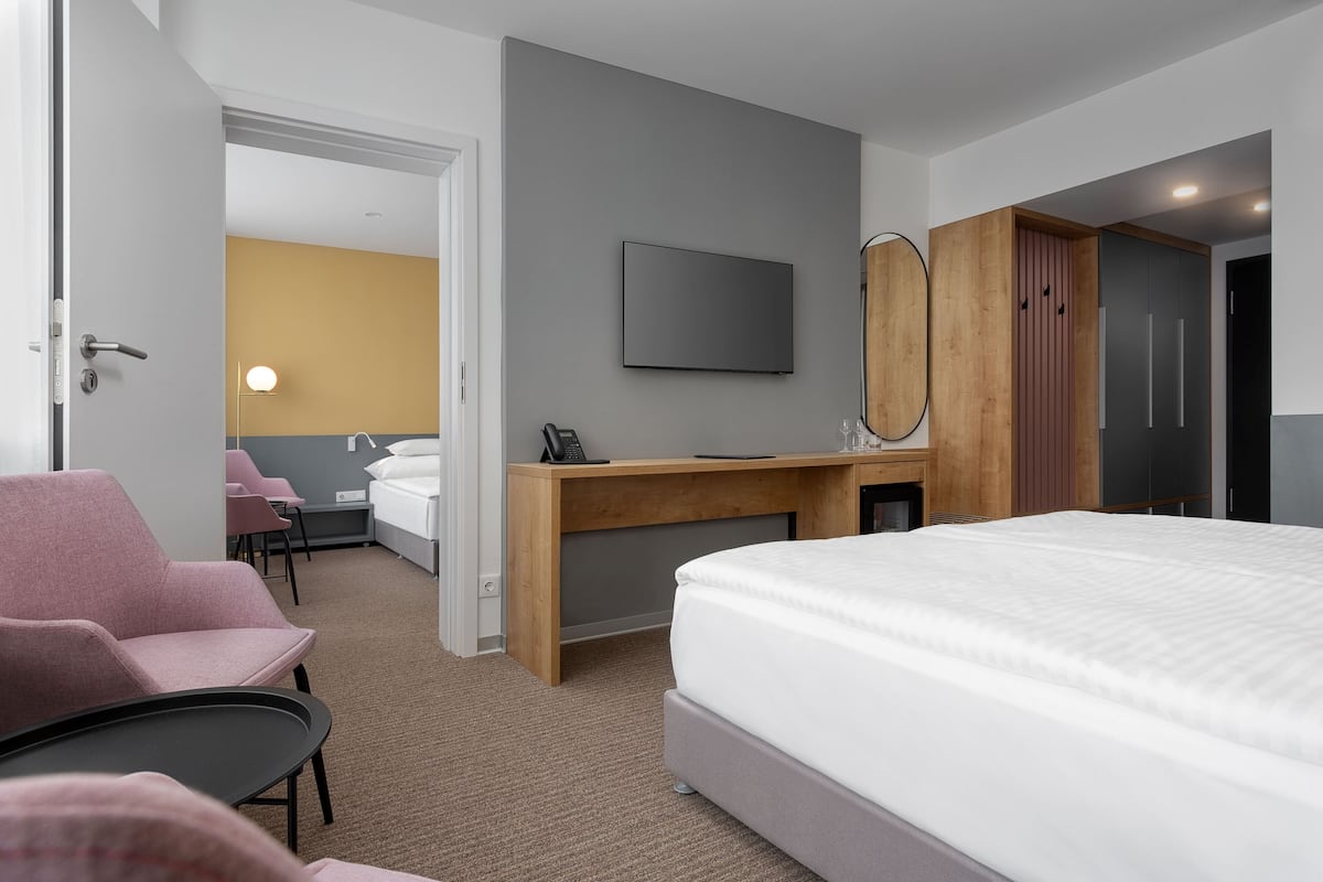 Quarto de hotel com cama, escrivaninha com espelho, televisão, cadeira e uma pequena mesa.