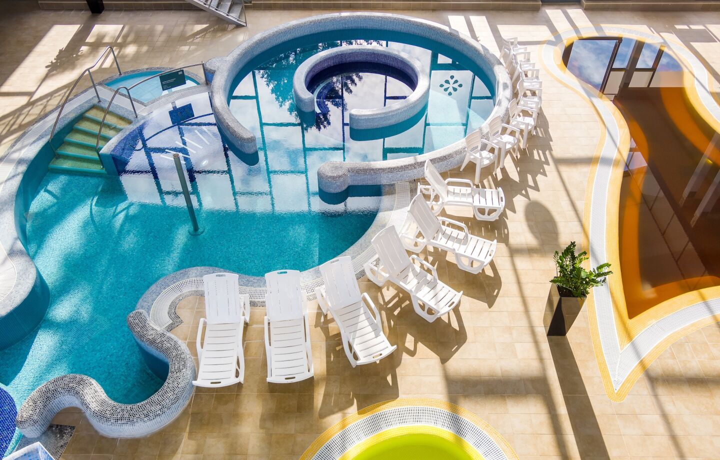 Una piscina grande y circular con un jacuzzi central, rodeada de sillones blancos y una terraza para tomar el sol.