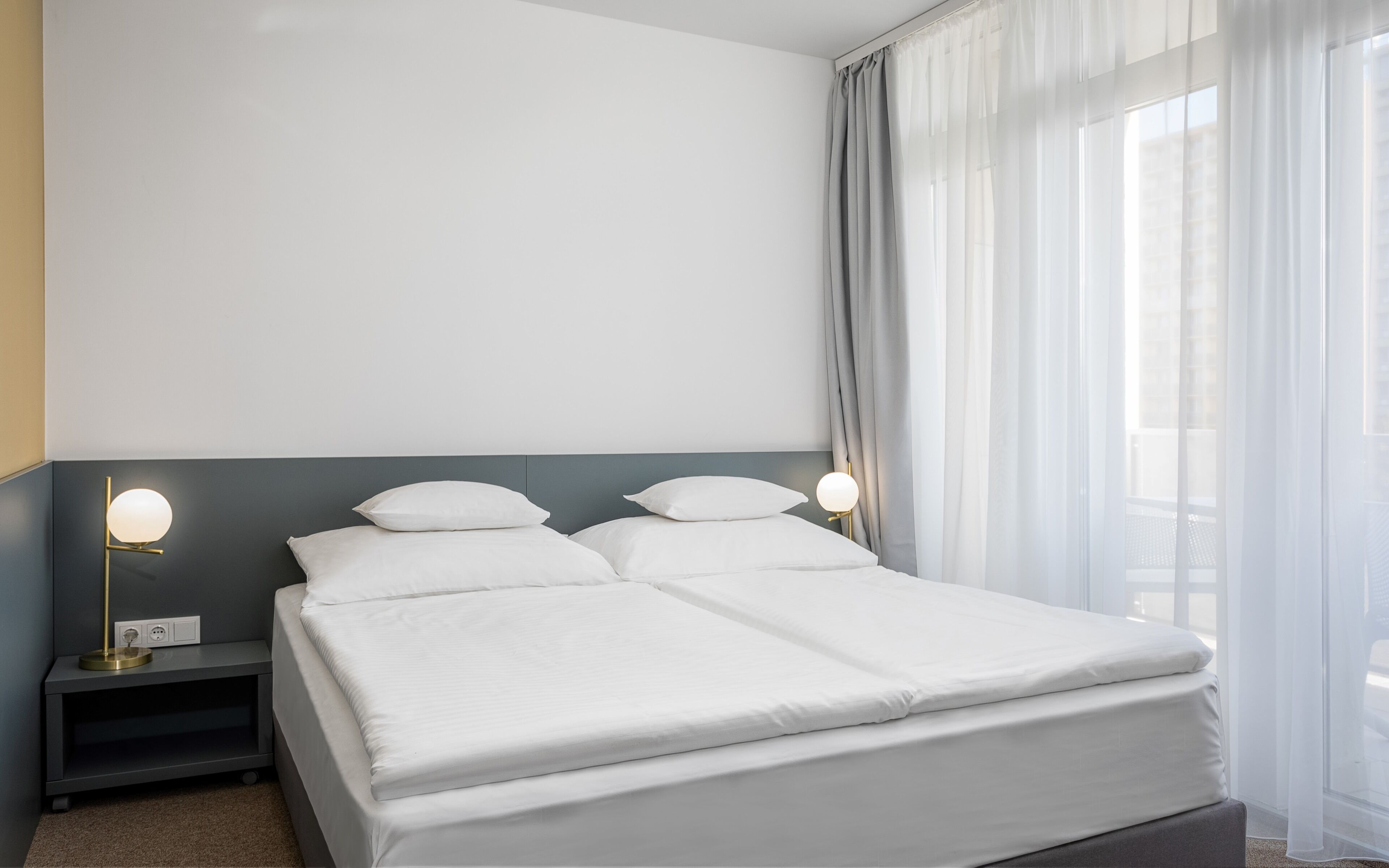 Un lit bien fait, avec du linge de lit blanc, dans une chambre d’hôtel moderne.