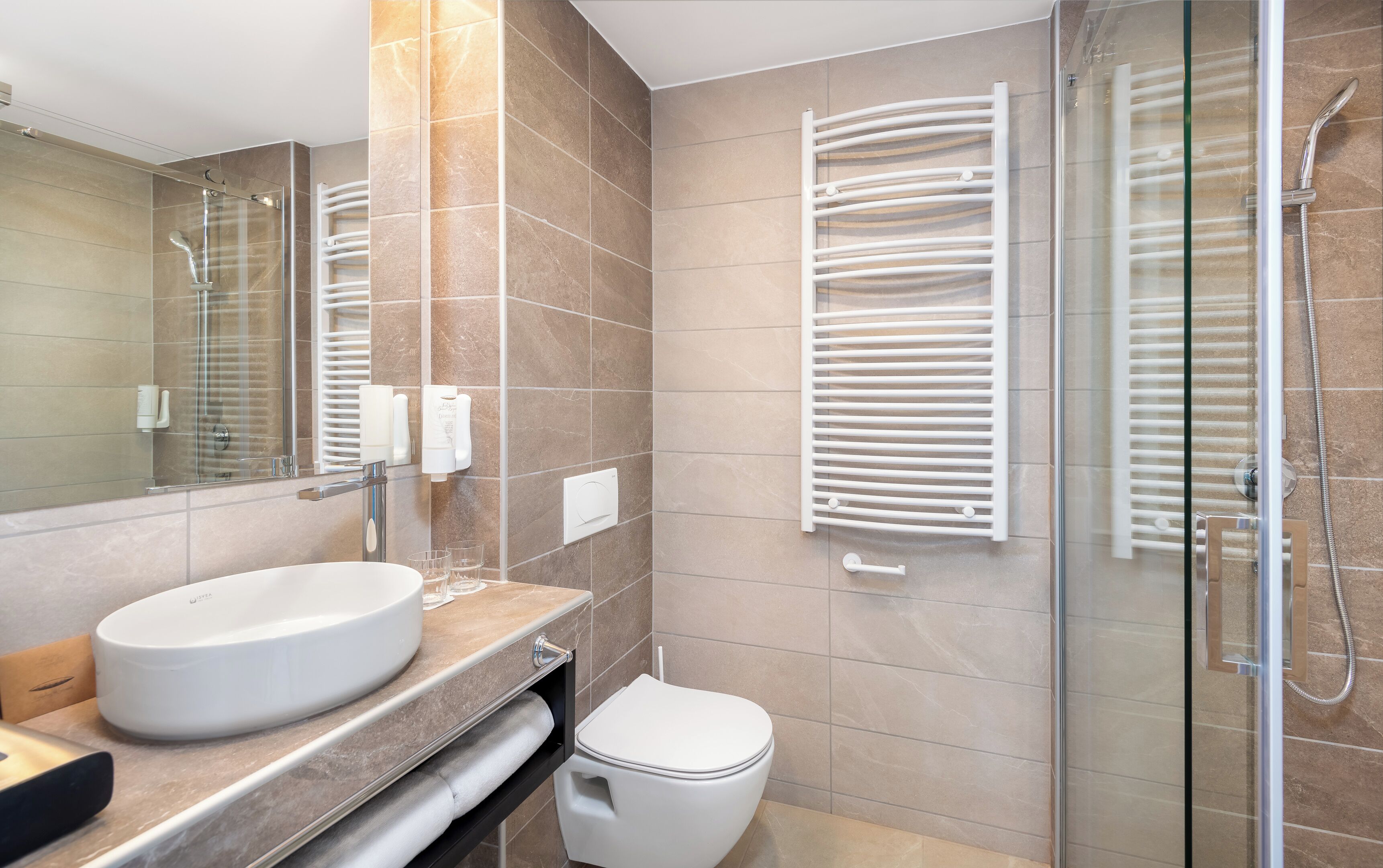 A modern bathroom with a large mirror, a round sink, a toilet, and a glass-enclosed shower area.