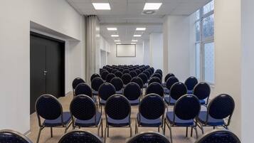Un salón de conferencias con filas de sillas y una pantalla para proyector al frente.