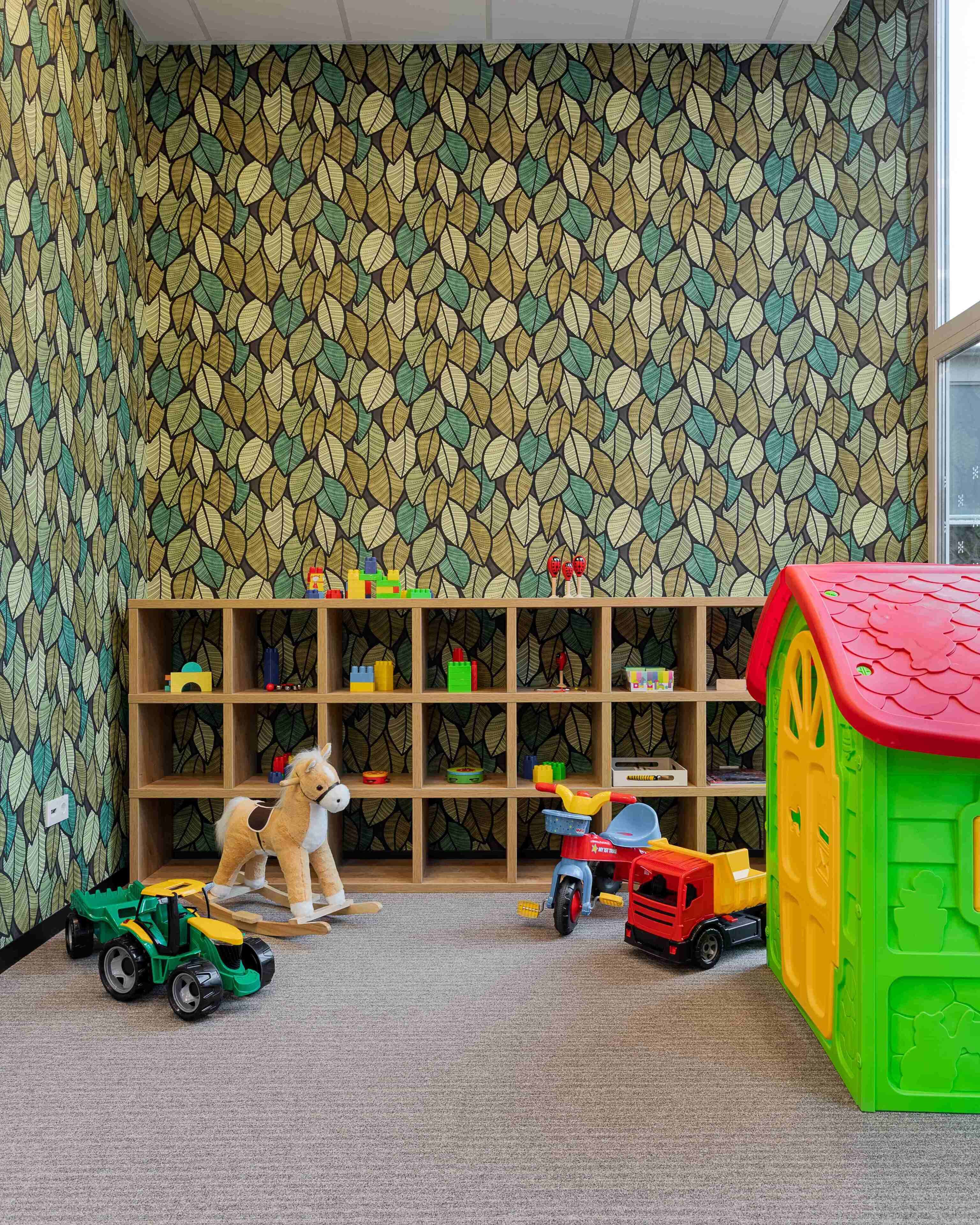 A playroom with a patterned wall, wooden shelves with toys, and a green playhouse.