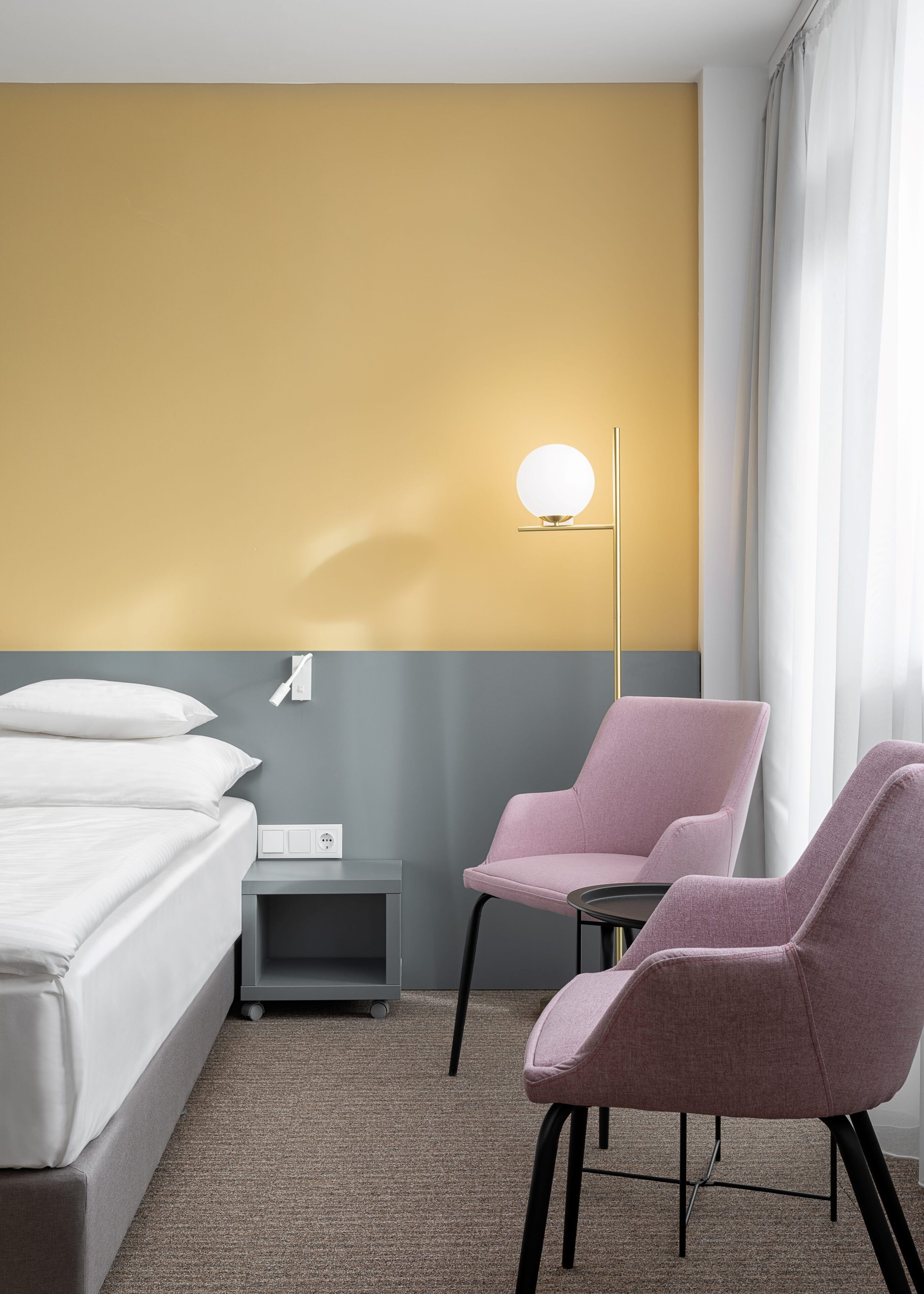 A hotel room with a bed, a nightstand, a lamp, and two chairs.