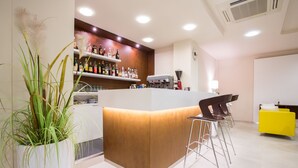 A reception area with a wooden counter, bar stools, a potted plant, and a yellow sofa. - Hotel Condor (Cervia)