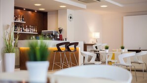 A modern bar area with stools, a coffee machine, and shelves of bottles. - Hotel Condor (Cervia)