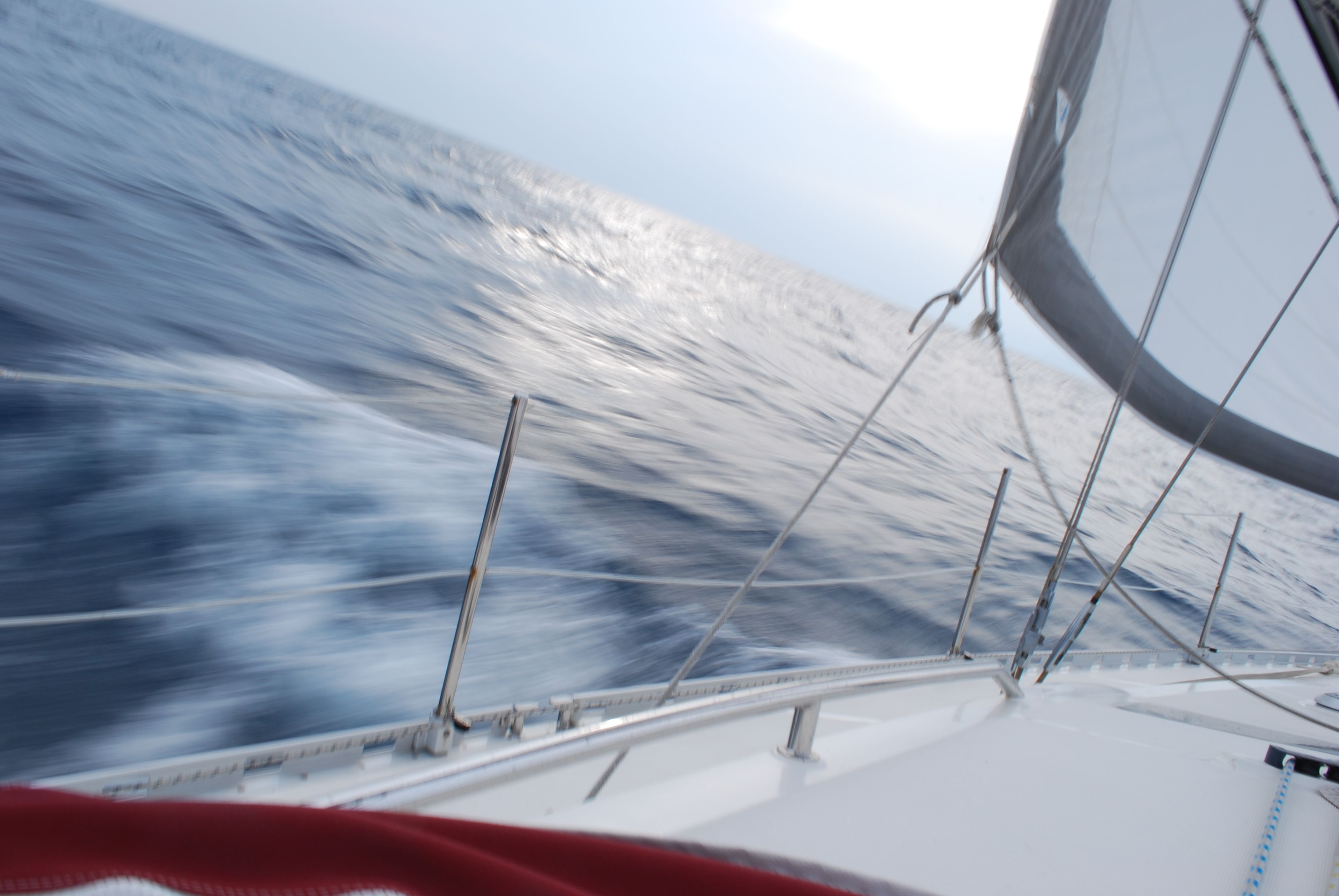 A view from a boat with a red and white sail, a metal railing, and the ocean in the background.