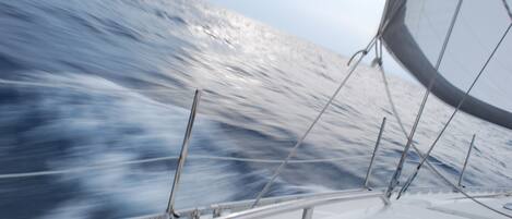 A view from a boat with a red and white sail, a metal railing, and the ocean in the background.