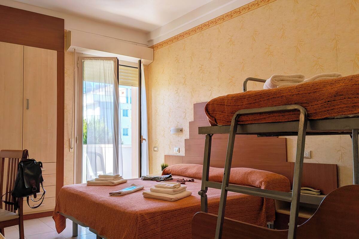 A dormitory room with bunk beds, a desk, a chair, and a wardrobe.