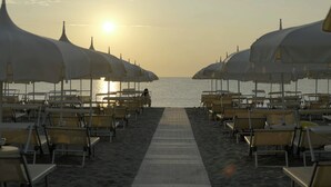 A beachside walkway with rows of sun umbrellas and beach chairs. - Hotel Condor (Cervia)