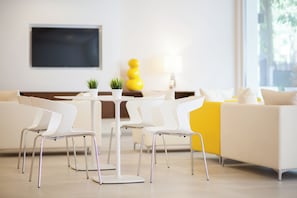 A modern living room with a white sofa, white chairs, a small table, a yellow decorative piece, and a TV mounted on the wall.
