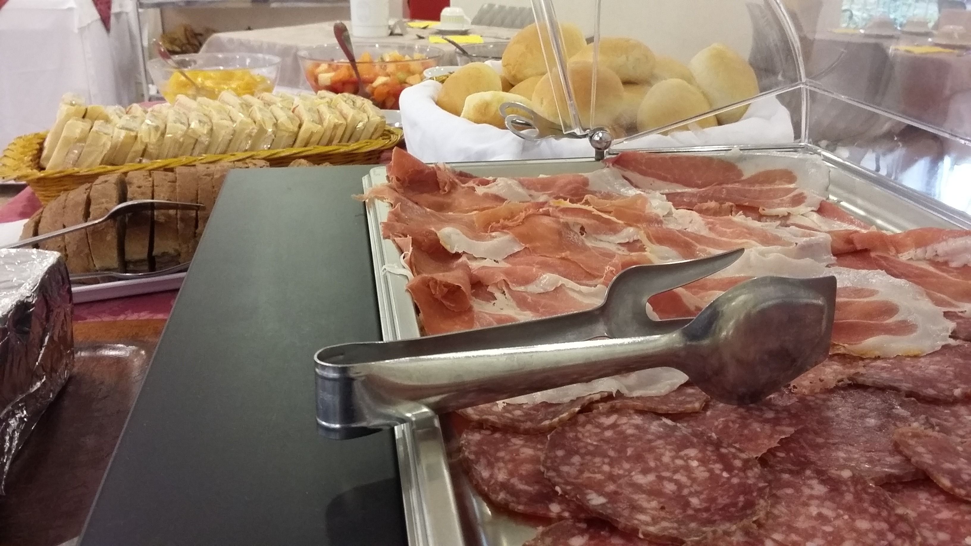 Buffet com diversos alimentos, incluindo carnes fatiadas, pão e frutas.