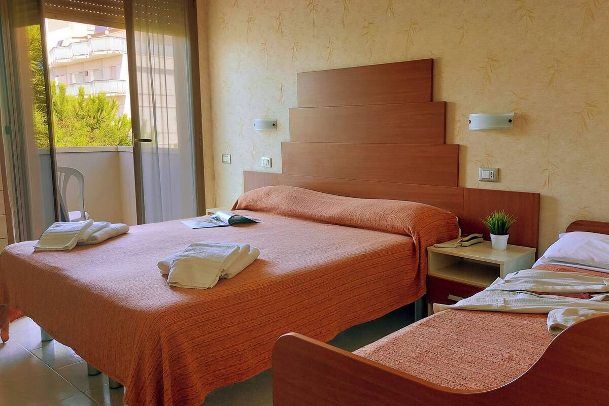 A hotel room with two beds, a nightstand, a small potted plant, and a view of a building outside.