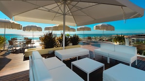 A deck with white lounge chairs and tables, umbrellas, and a view of the ocean. - Hotel Condor (Cervia)