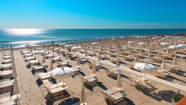 A beach with rows of sun loungers and umbrellas, a clear blue sky, and the ocean in the background. - Hotel Condor (Cervia)