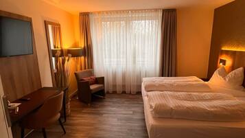 Habitación de hotel con cama, escritorio, silla, televisor y ventana con cortinas.