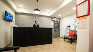 A reception area with a black reception desk, a television mounted on the wall, a fire alarm, and a poster on the wall. - Hotel Highway Residency (Mumbai)