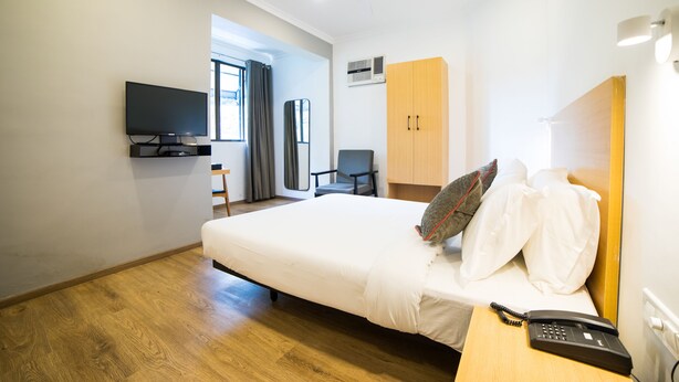 A hotel room with a bed, a desk with a telephone, a television mounted on the wall, a wardrobe, and a ceiling fan. - Hotel Highway Residency (Mumbai)