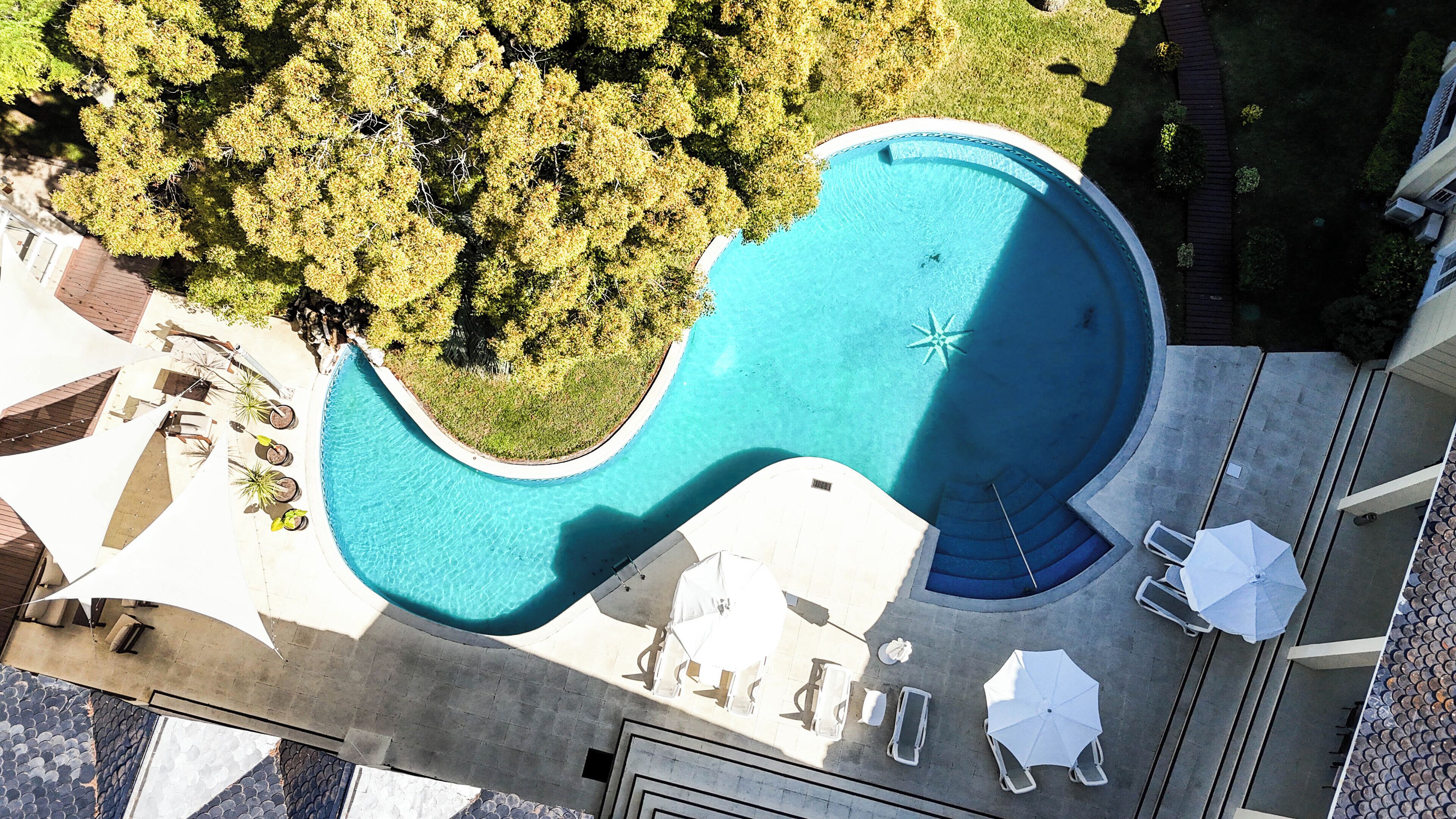 An aerial view of a swimming pool with a unique shape, surrounded by greenery and outdoor seating.