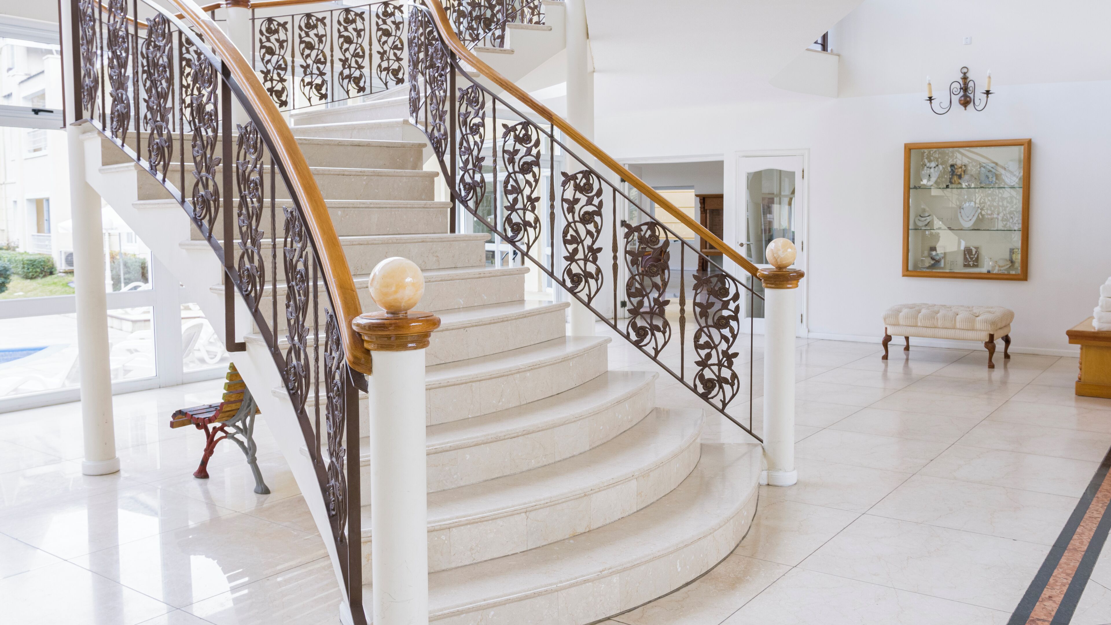 Una gran escalera con barandillas de metal ornamentadas y columnas blancas, que conduce a un piso superior.