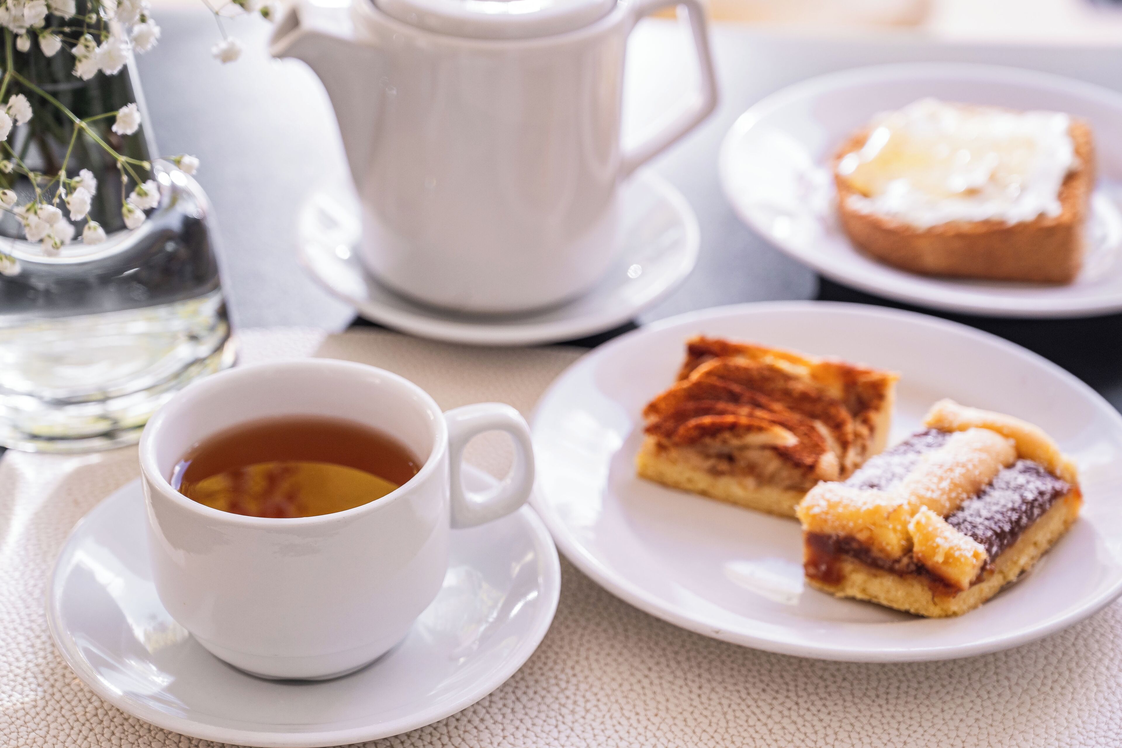 Una mesa servida con una taza de té, una tetera, una jarra y dos platos con pasteles.