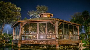 A wooden gazebo with a glass enclosure, situated over a pond, surrounded by trees and a clear night sky. - Parque Hotel Jean Clevers (Punta del Este)