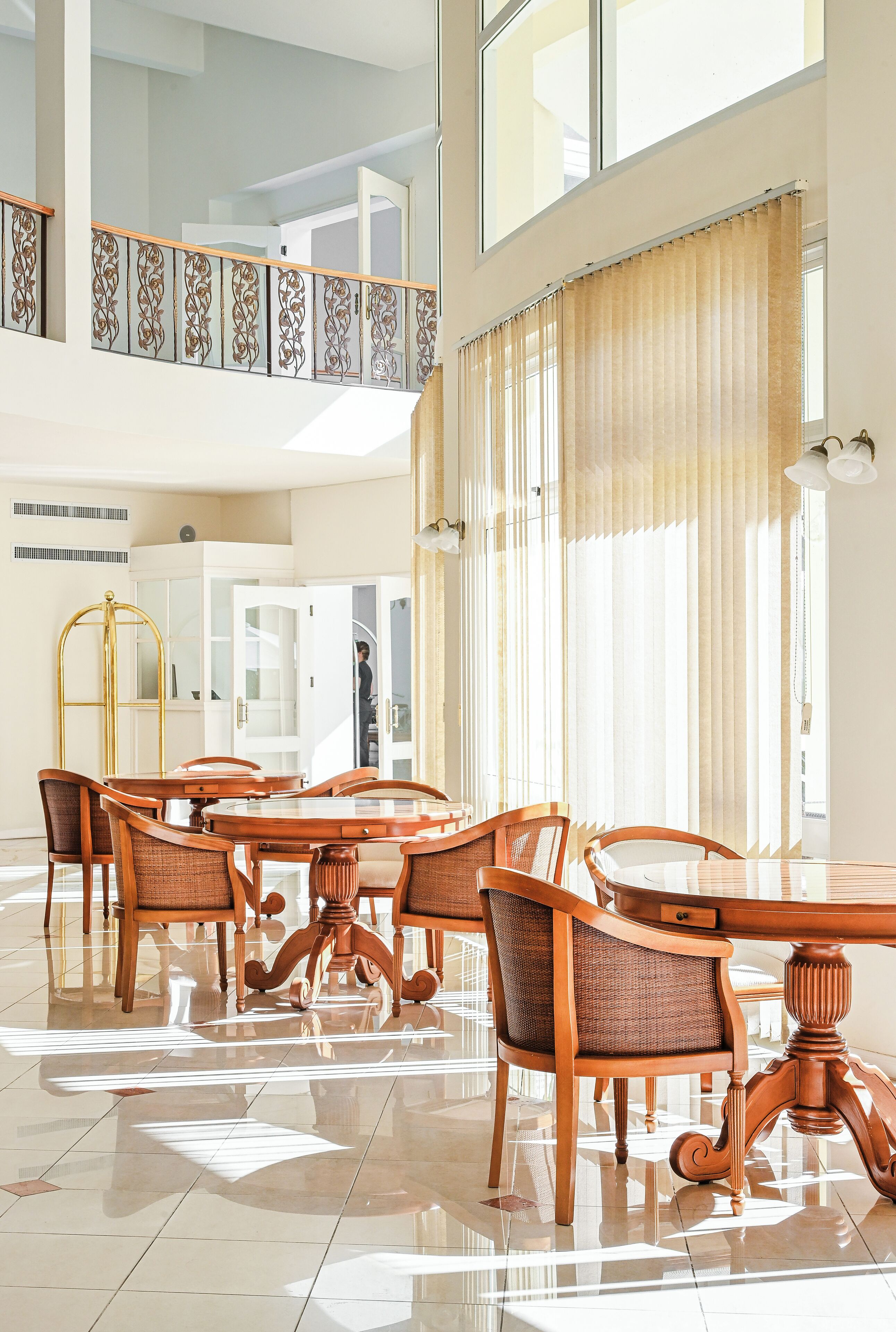 A spacious dining area with a high ceiling, large windows, and a view of the upper floor.