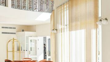 A spacious dining area with a high ceiling, large windows, and a view of the upper floor.