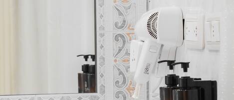 A bathroom with a white hairdryer mounted on the wall, a white tissue box on the counter, and a mirror reflecting the bathroom's decor.