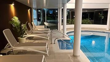 Un área de piscina interior con sillones de descanso y una planta en maceta.