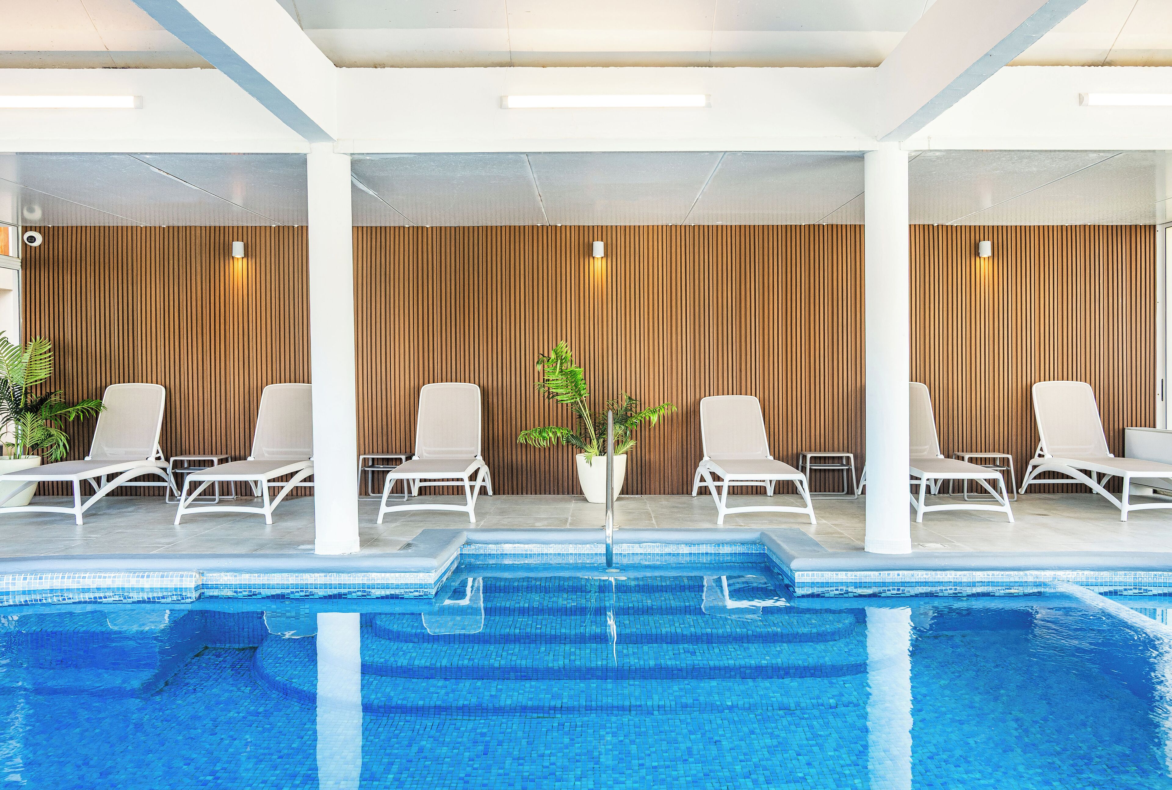 A modern indoor pool area with white lounge chairs and a wooden wall.