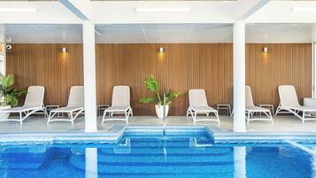 A modern indoor pool area with white lounge chairs and a wooden wall.