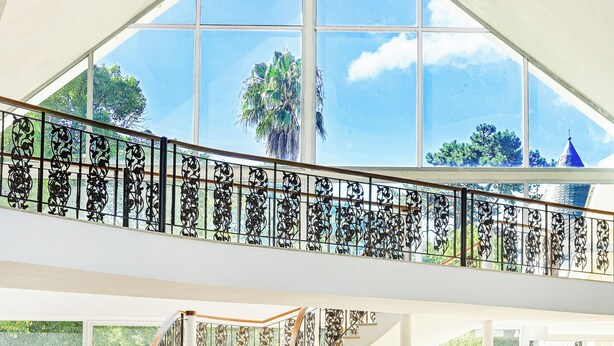A spacious interior with a high ceiling, a central staircase, and large windows offering a view of the outdoors. - Parque Hotel Jean Clevers (Punta del Este)