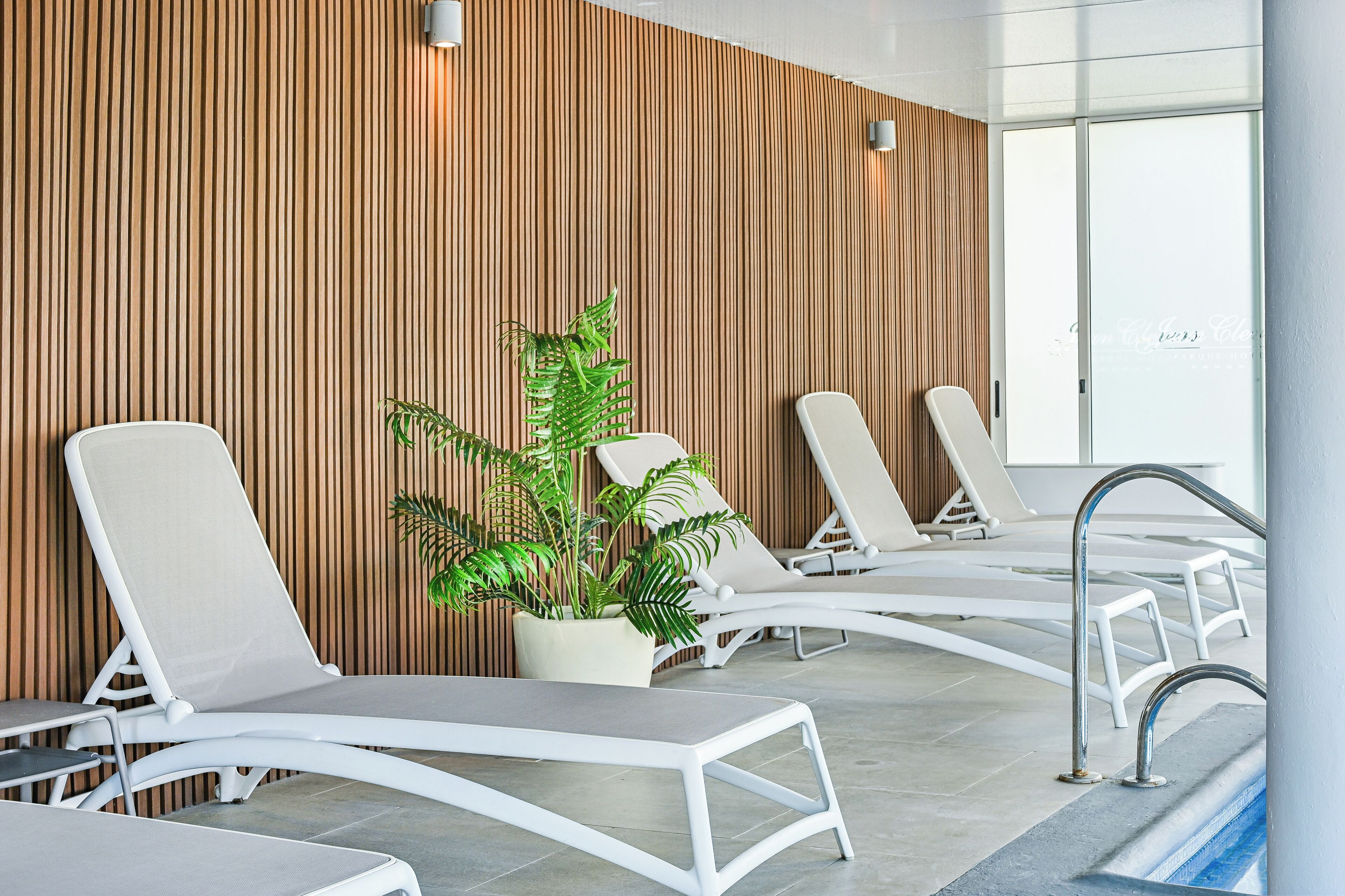 Un área de piscina interior moderna con sillones blancos y una planta en maceta.
