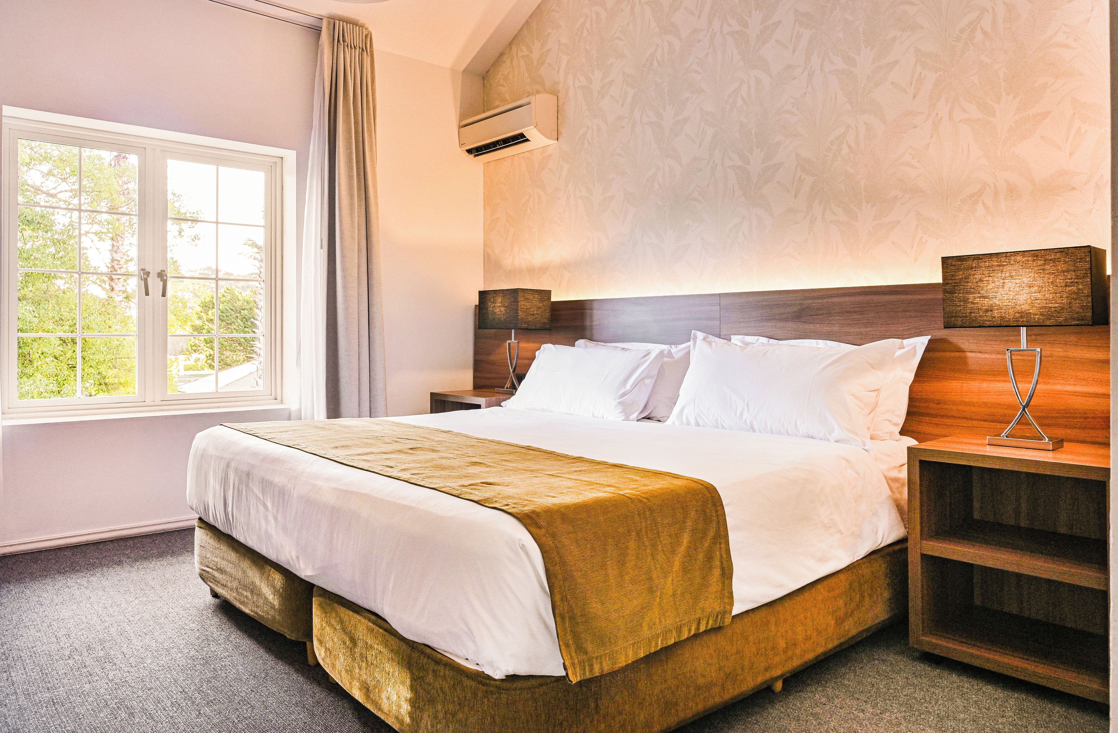 A hotel room with a bed, bedside tables, a lamp, and a window with curtains.
