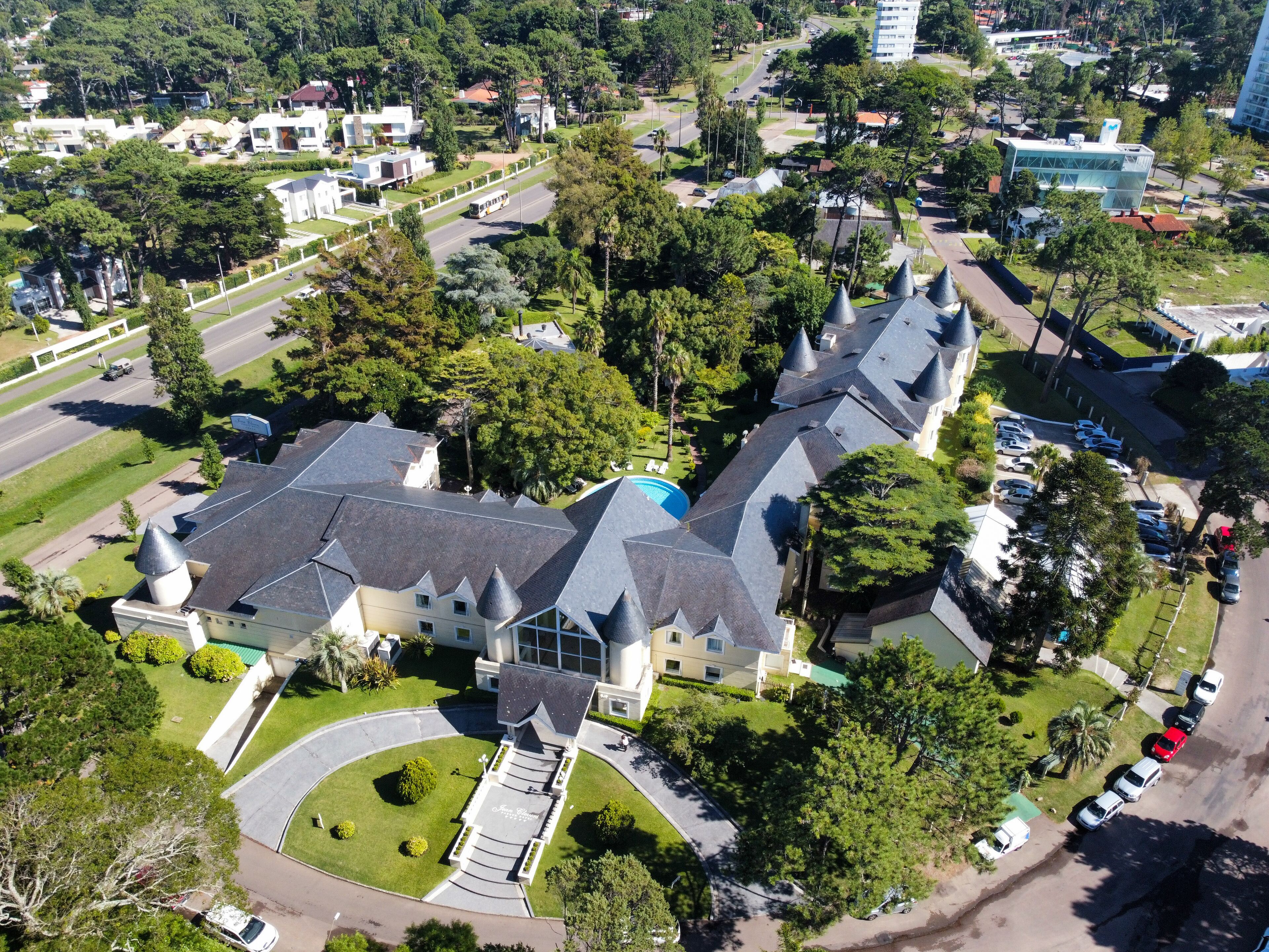 An aerial view of a residential area with a large, multi-story house featuring a prominent turret and a swimming pool.