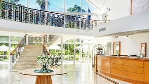 A spacious lobby with a marble staircase, a reception desk, and large windows offering views of greenery. - Parque Hotel Jean Clevers (Punta del Este)