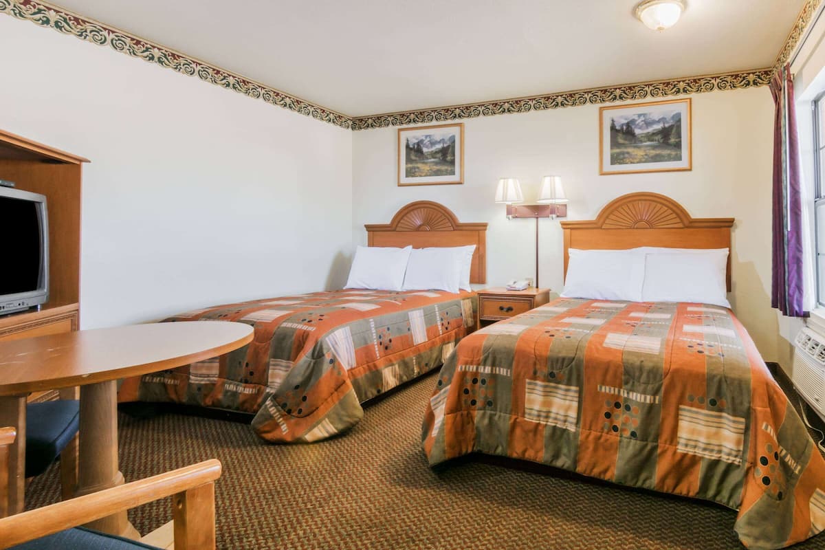 Ein Hotelzimmer mit zwei Betten, einem Fernseher, einem Tisch und zwei Lampen.