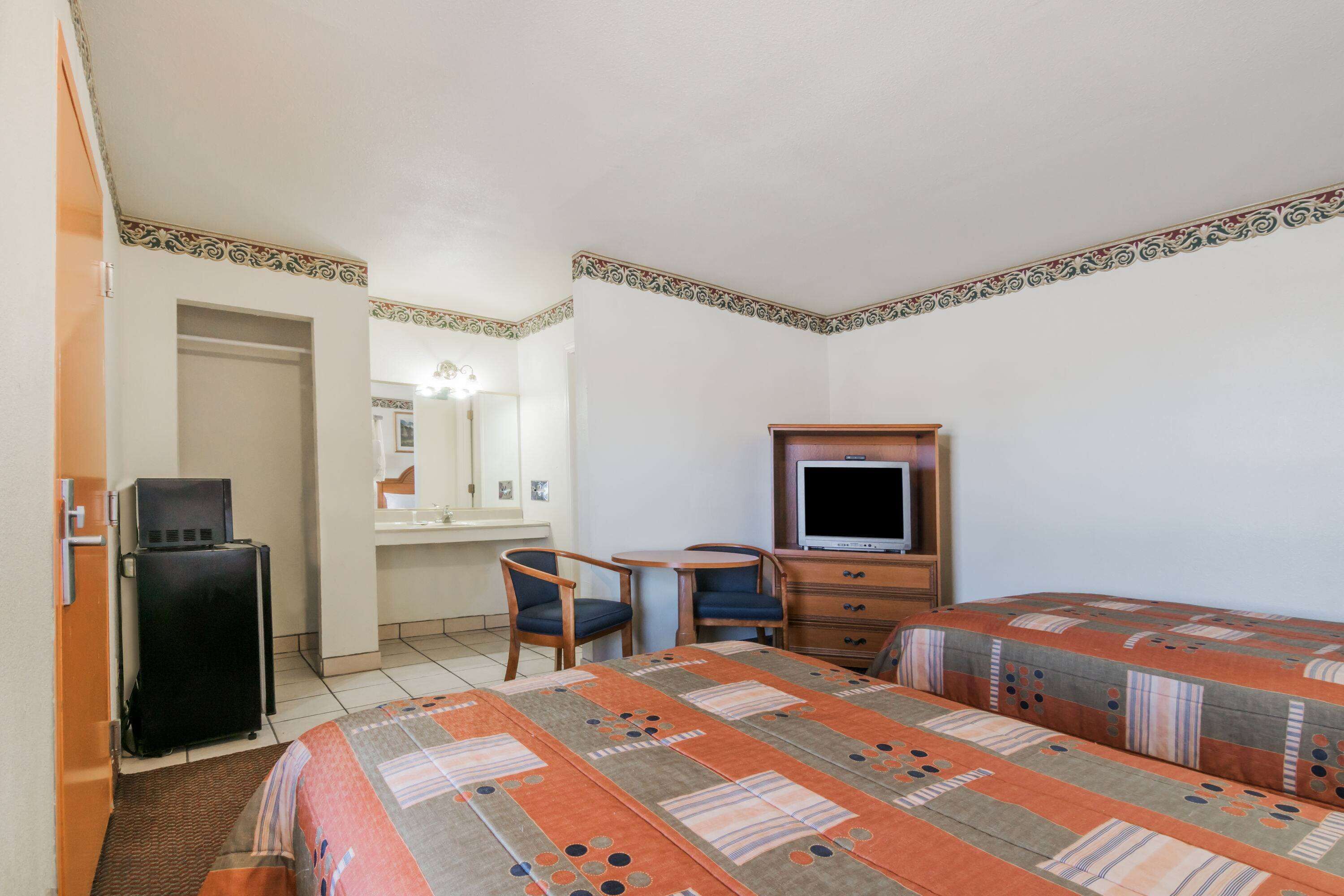 Una habitación de hotel con dos camas, un escritorio con silla, televisor y armario.