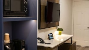 Una cocina compacta con microondas, cafetera y un pequeño cubo de basura.